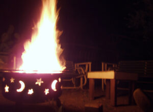 A fire pit burning brightly on a patio on a warm evening with garden seating nearby