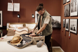 A person packing a suitcase with a sun hat and clothing on a bed in a bedroom