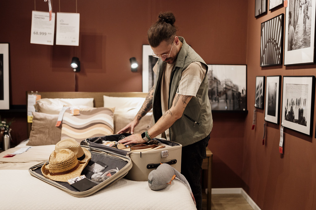 A person packing a suitcase with a sun hat and clothing on a bed in a bedroom